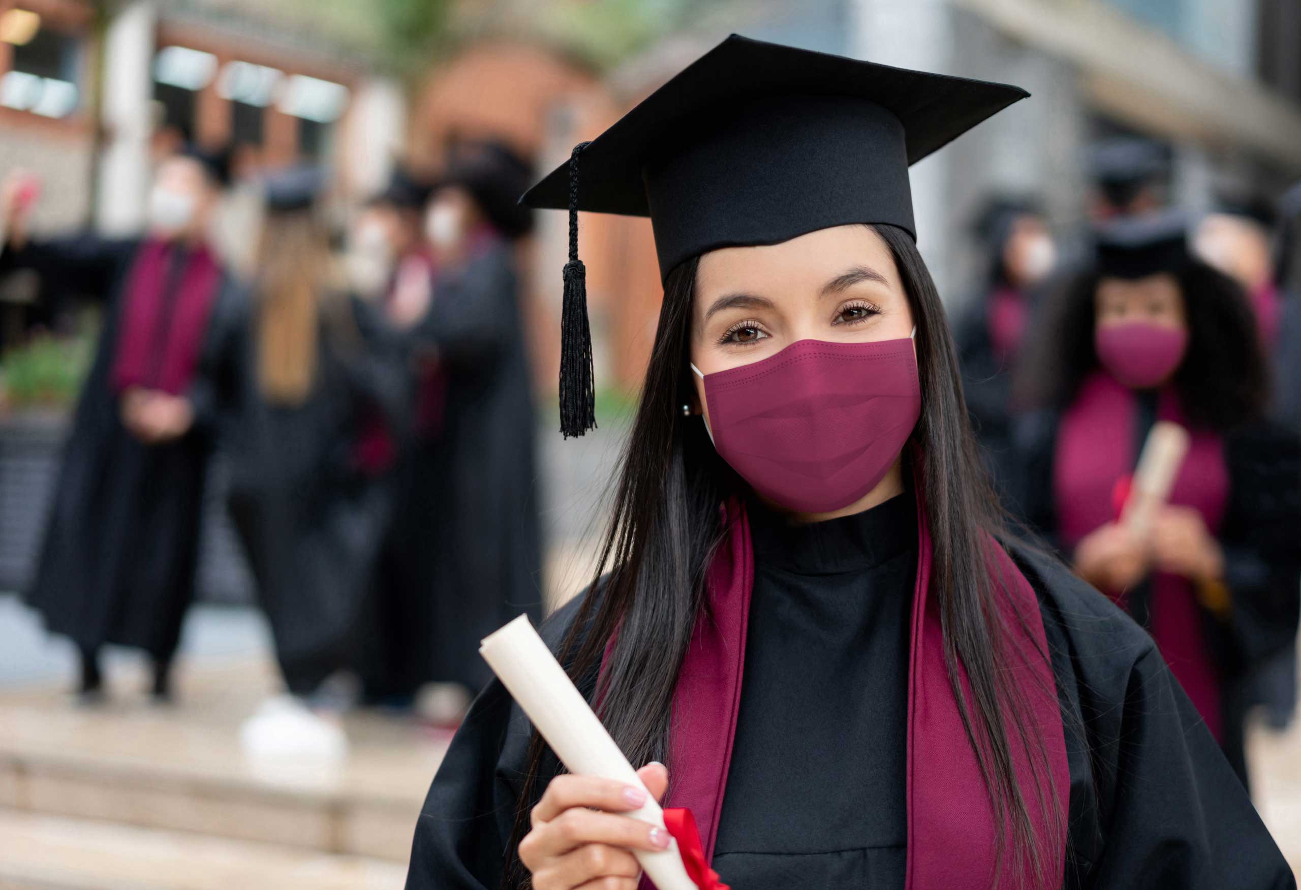 2021 graduates job search; graduate in cap and gown, wearing a mask for COVID safety, while holding diploma